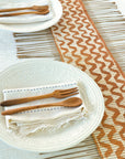 A brown and white decorative table runner with two plates napkins, and utensils on top