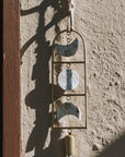 Decorative wind chime with moon phases and a bell on a textured wall.