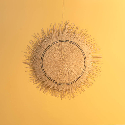 A woven wall decor resembling a sun with a central brown circle and spiky extensions, hanging against a yellow background.