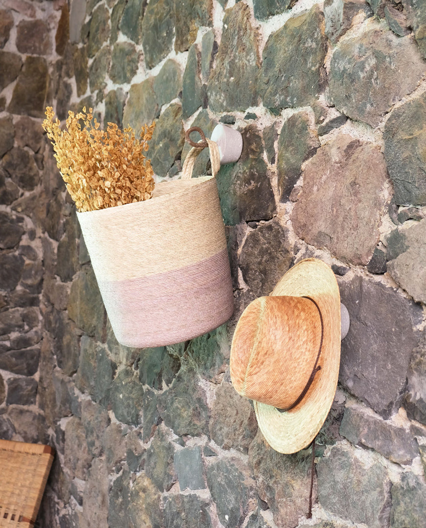 Woven basket and hat hanging on a stone wall.