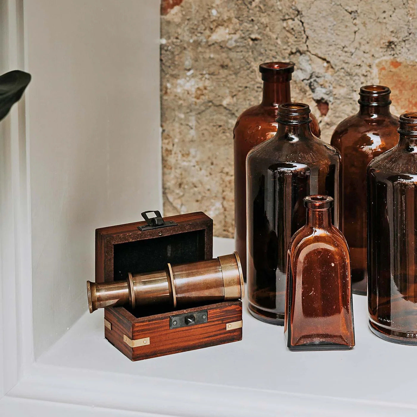 Collection of brown bottles and a wooden box with a telescope on a white surface.