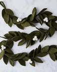 Two green leaf garlands with white berries on a light gray background