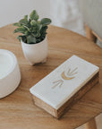 Rectangular wooden block with a decorative design on a wooden surface with a plant and candle