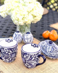 Blue and white ceramic mugs with floral patterns on a table with flowers and oranges.