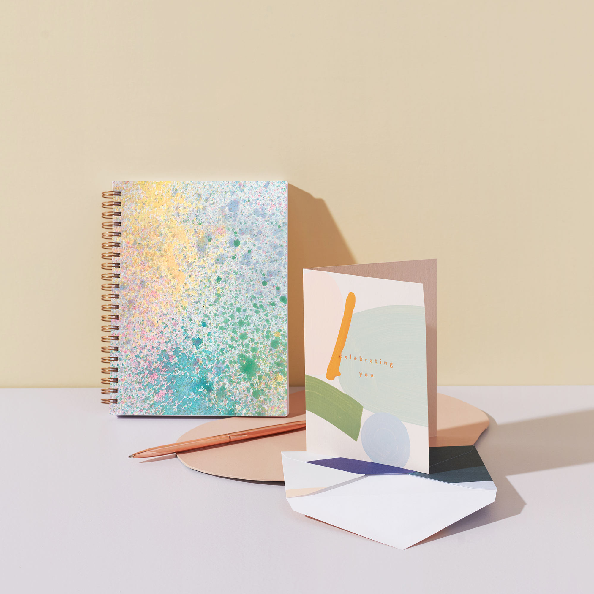 Notebook with colorful cover and a card on a light surface with a beige background