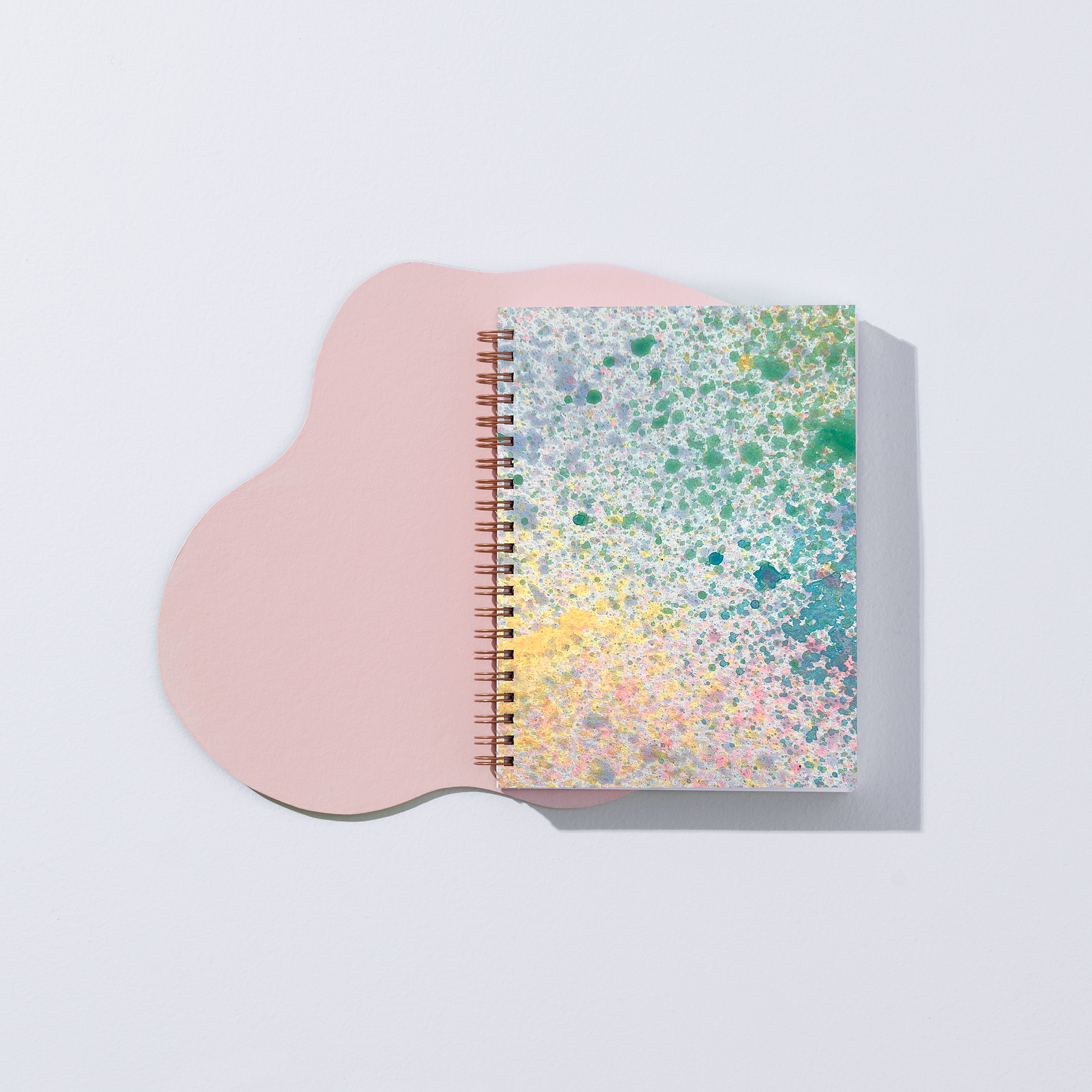 Notebook with colorful splatter design on a pink stand against a light gray background