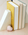 A pair of handmade stone bookends with a pentagonal shape with three books in-between and a heart shaped paperweight next to them