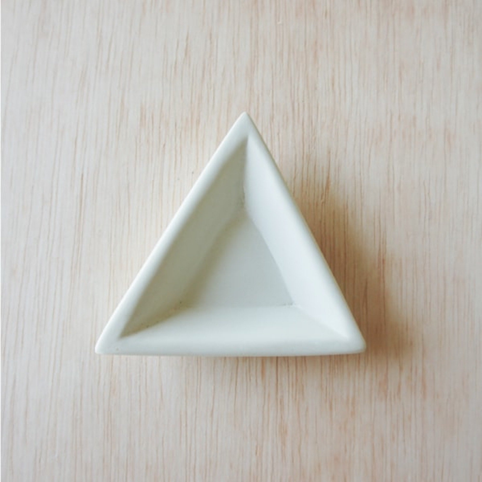 A natural stone mini triangle dish, hand carved and smoothed, placed on a beige surface