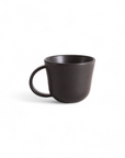 A matte black stoneware mug with a handle, on a plain background