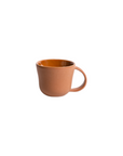 A terracotta colored stoneware mug with a handle, on a white background