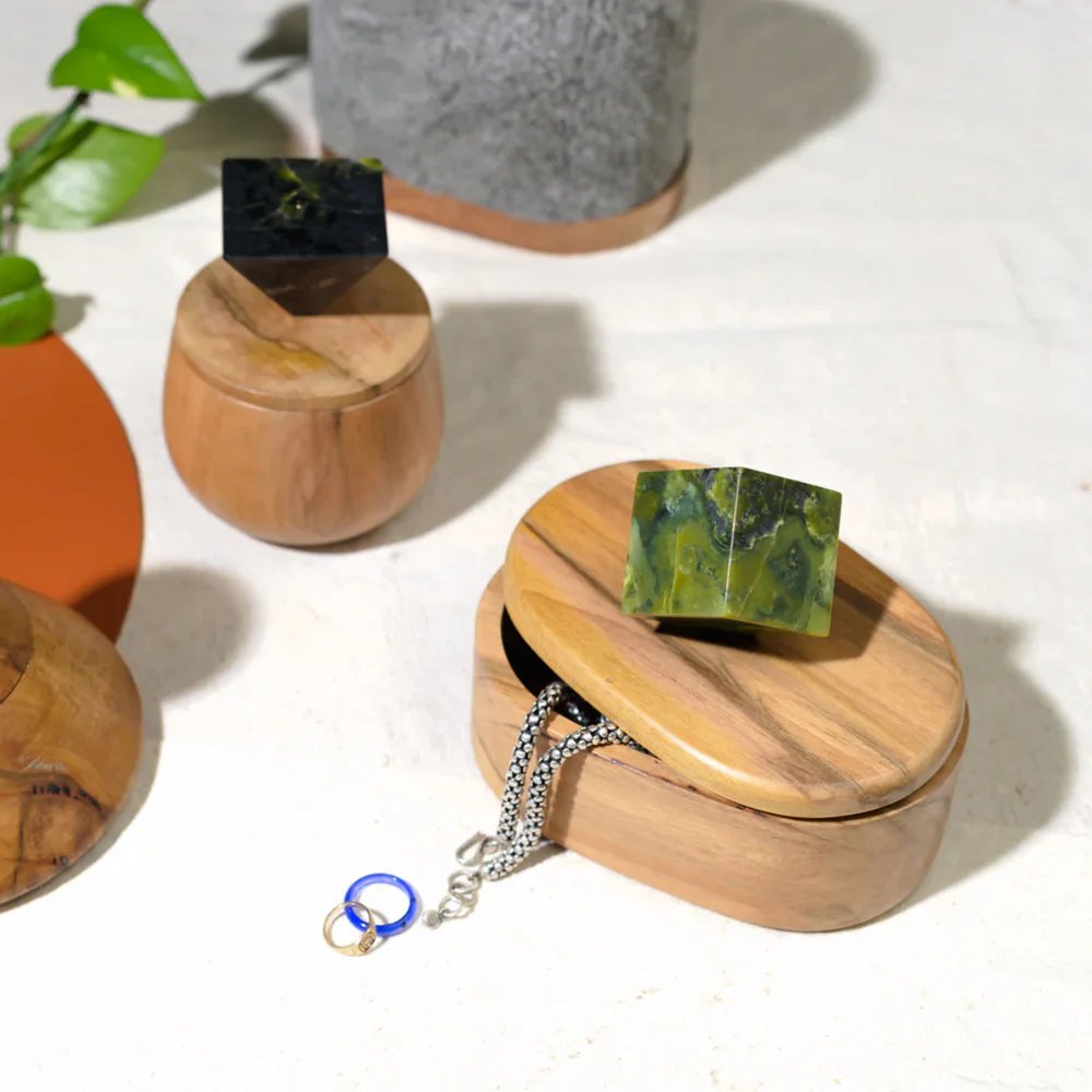 Wooden jewelry box with a green stone on top, surrounded by other decorative items.