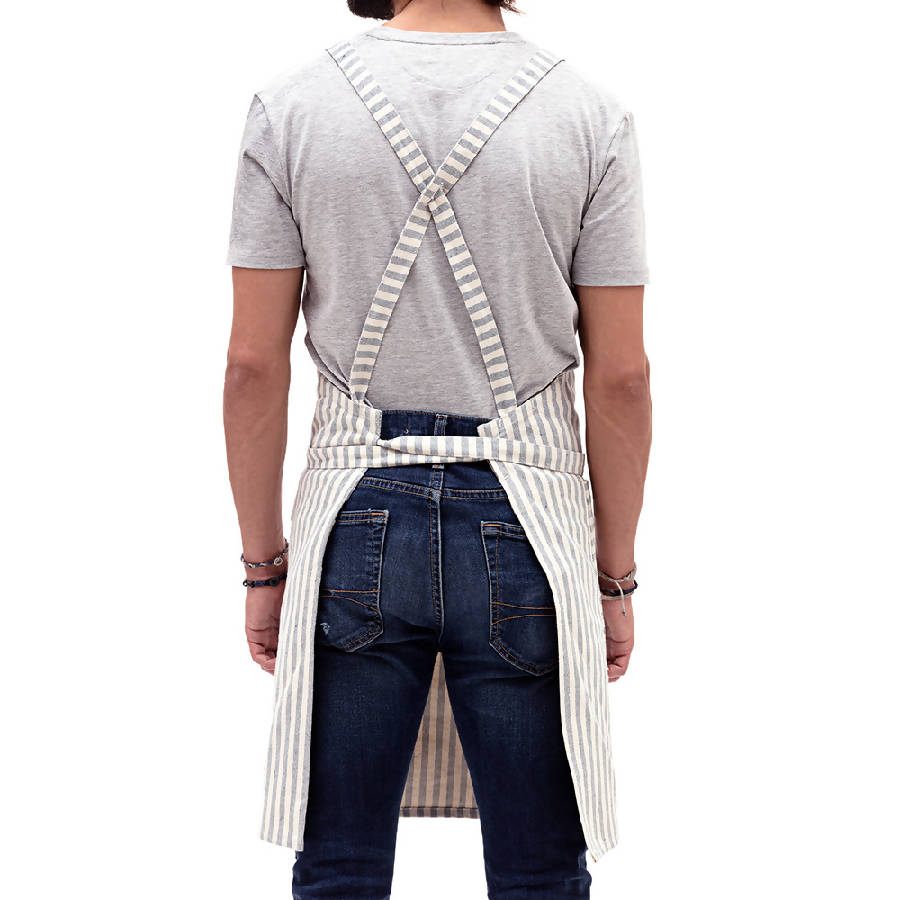 A person showing the backside of a striped crossback bib apron with multiple pockets and a utility loop.