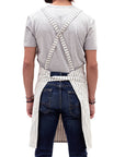 A person showing the backside of a striped crossback bib apron with multiple pockets and a utility loop.