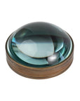 A round paperweight with a magnifying glass in antique brass color, featuring a glass center and a metallic brass outer ring.