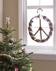 A peace wreath with white decorations hanging inside near a window next to a christmas tree