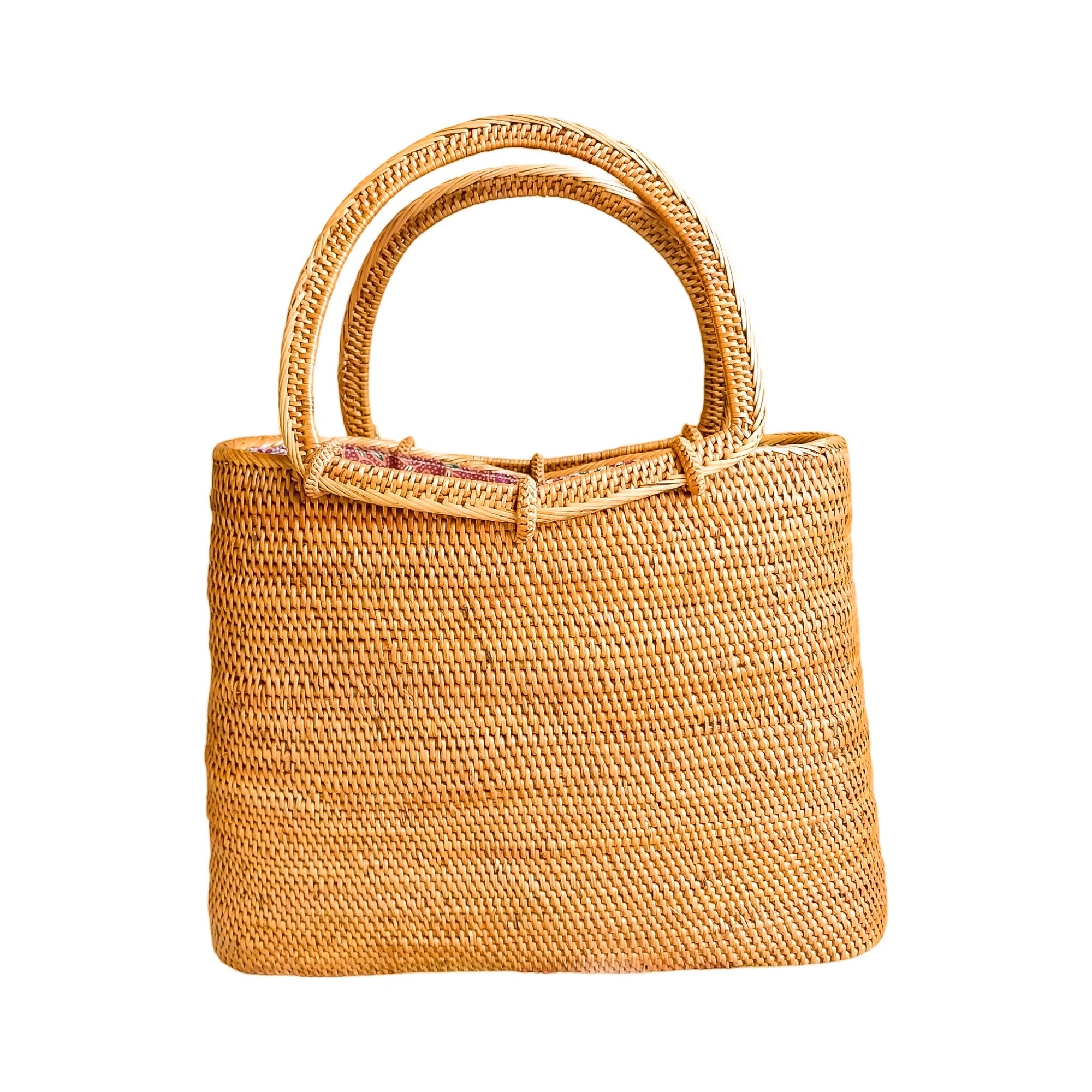 A beige rattan tote handbag with top handles and a drawstring top closure, featuring a batik print fabric lining.