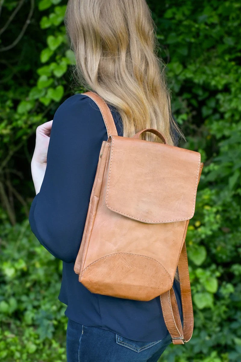 Person wearing a tan leather backpack against a green leafy background