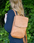 Person wearing a tan leather backpack against a green leafy background
