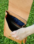 Hand holding a tan leather bag against a grassy background