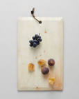 A wooden serving board with a hanging loop at the top. The board is adorned with an assortment of food items including a bunch of grapes, an olive, and a few nuts
