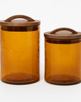 Two amber glass canisters with wooden lids on a white background