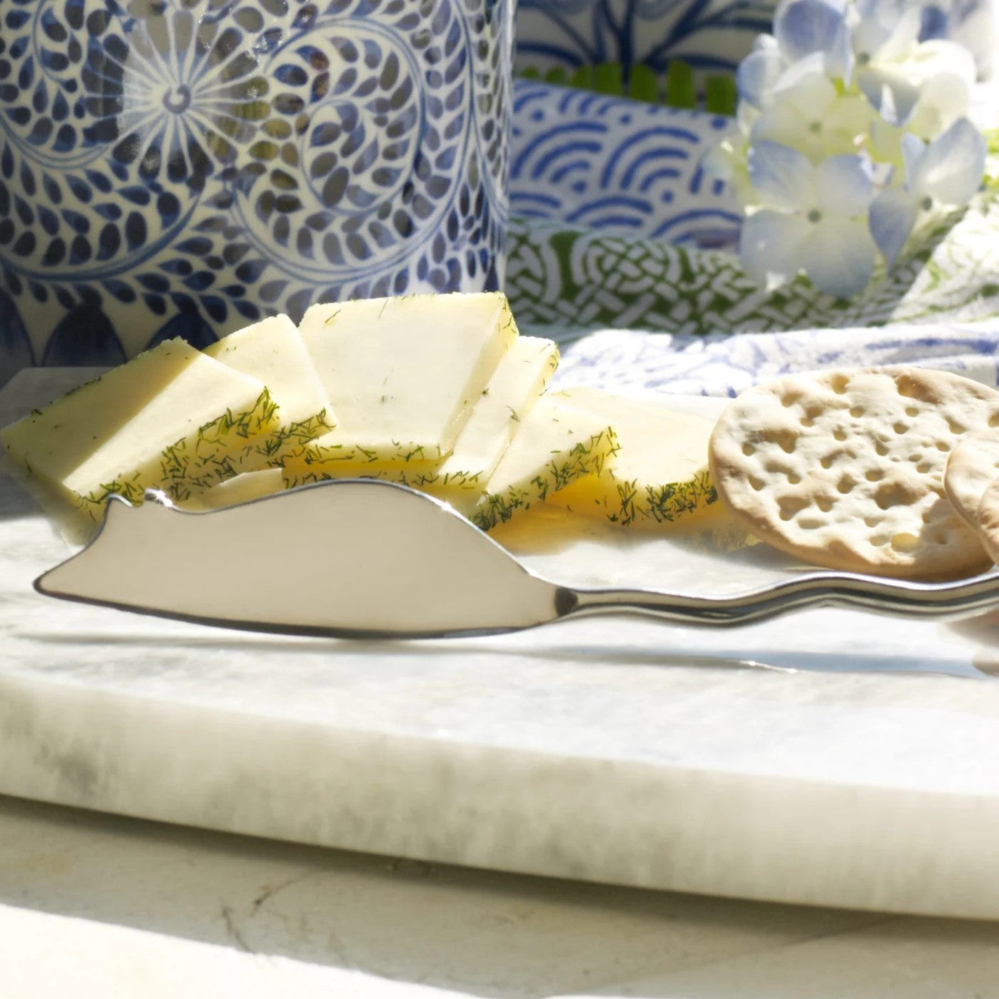 Cheese platter with sliced cheese, crackers, and a silver knife on a marble surface