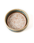 A terracotta bread warmer with a snowflake design, encased in a woven grass basket with blue dyed palm wrap details.