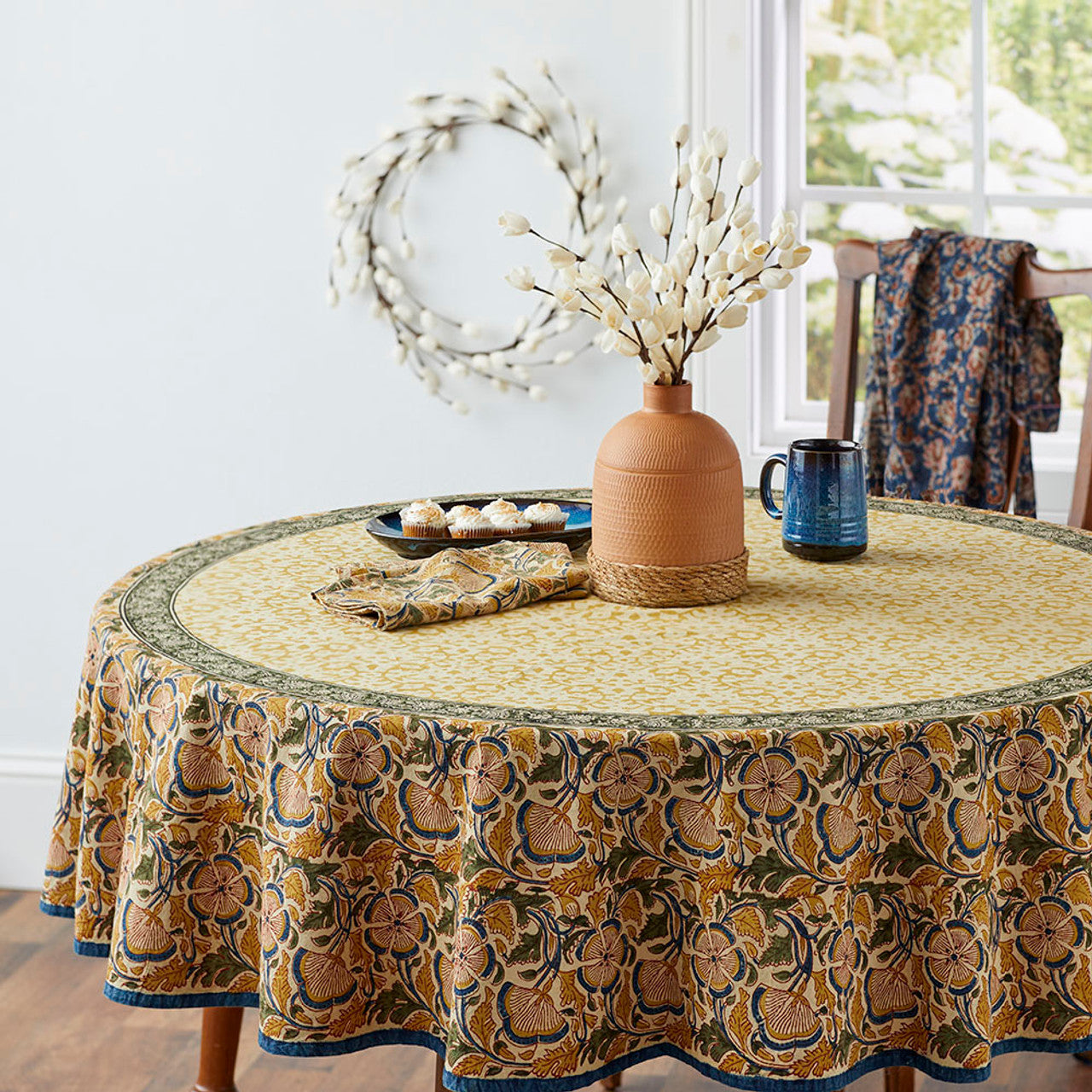 A round white sola wreath in the background of a room that has a table and dried flowers in a vase