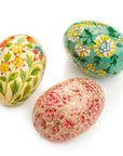 A set of three hand-painted wooden eggs, each with a different floral pattern, in green, white, and pink colors