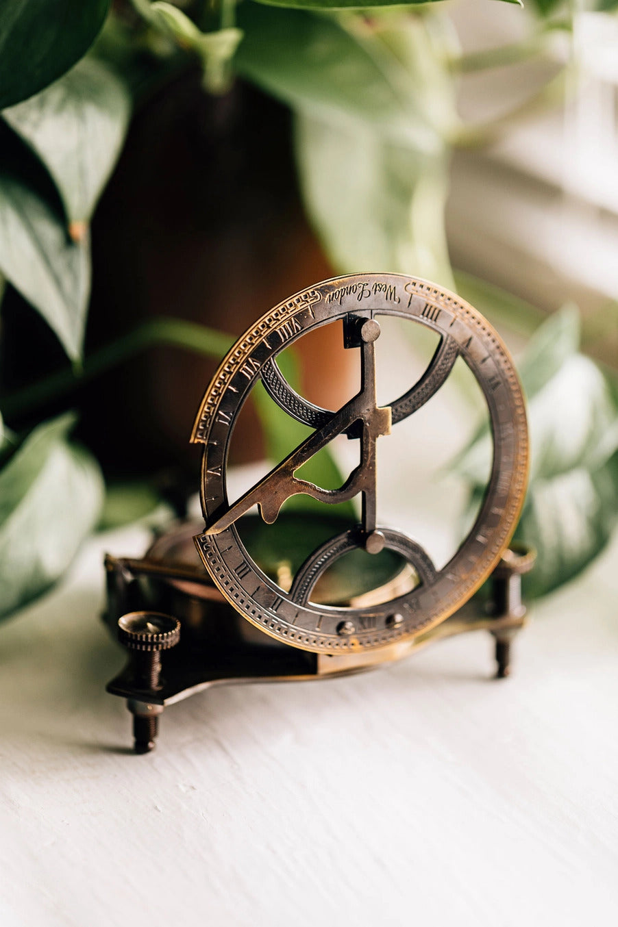 Vintage-style astrolabe on a white surface with greenery in the background