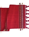 A red handwoven table runner with an arrow motif and fringe detail, laid out flat