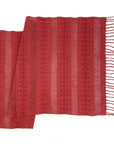 A terracotta-colored table runner with a striped pattern and fringed ends, laid out flat