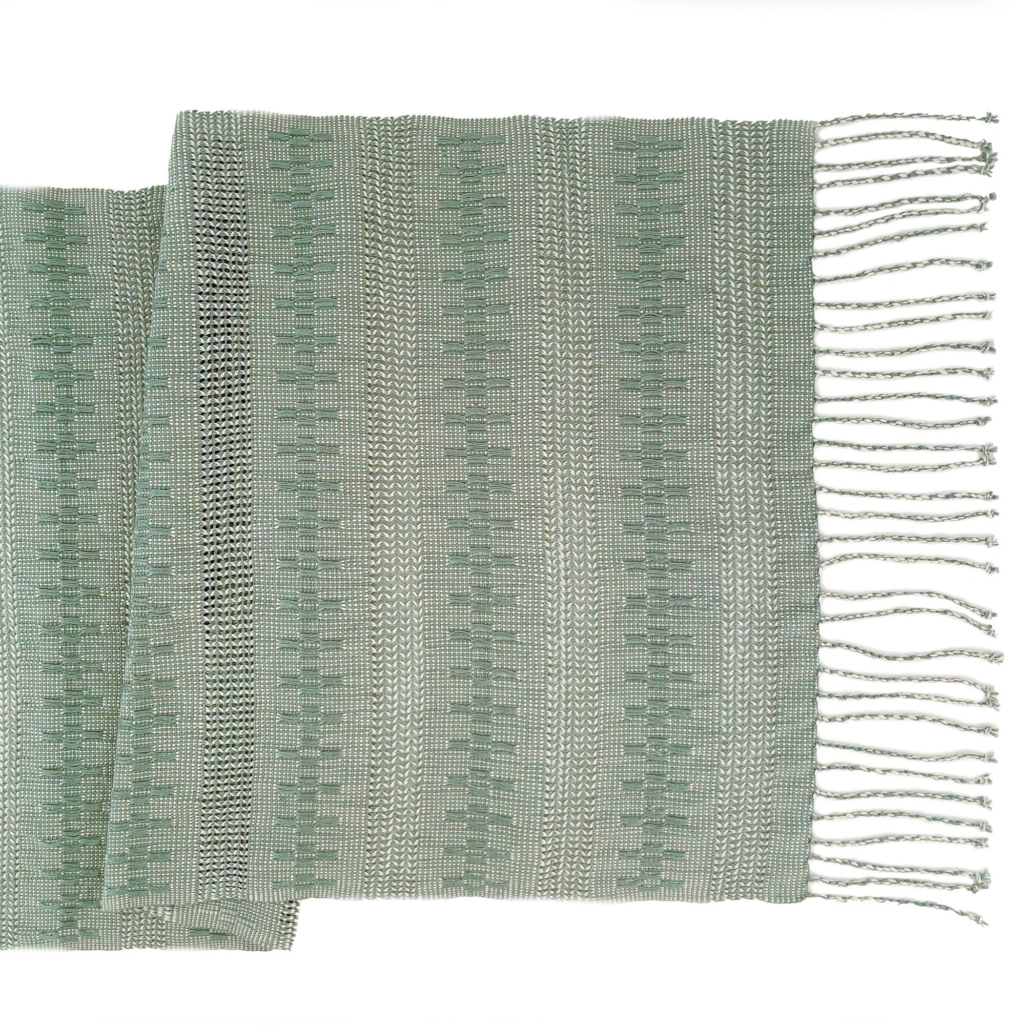 A sage green and white woven table runner with fringe, featuring a textured weave pattern