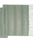 A sage green and white woven table runner with fringe, featuring a textured weave pattern