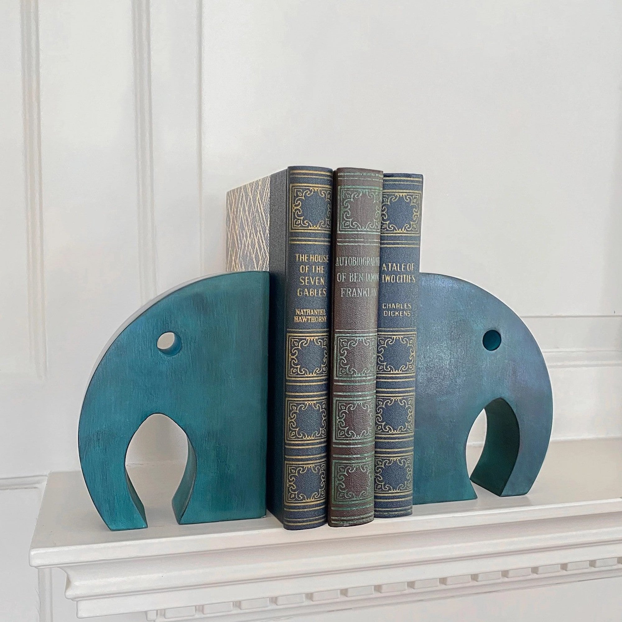 A pair of teal colored stone elephant bookends holding three books