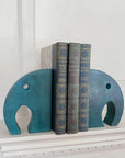 A pair of teal colored stone elephant bookends holding three books