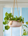 A ceramic planter hanging from the ceiling with a dried plant hanging off the edges