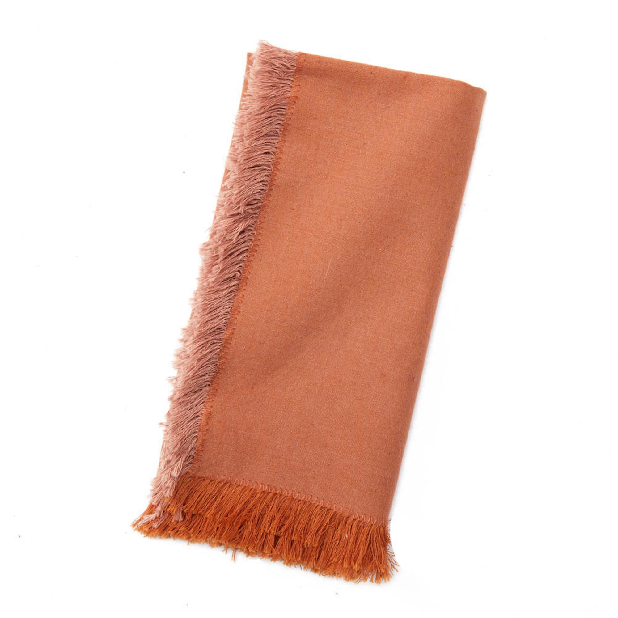 A woven terracotta orange napkin with frayed edges on a white background