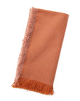 A woven terracotta orange napkin with frayed edges on a white background