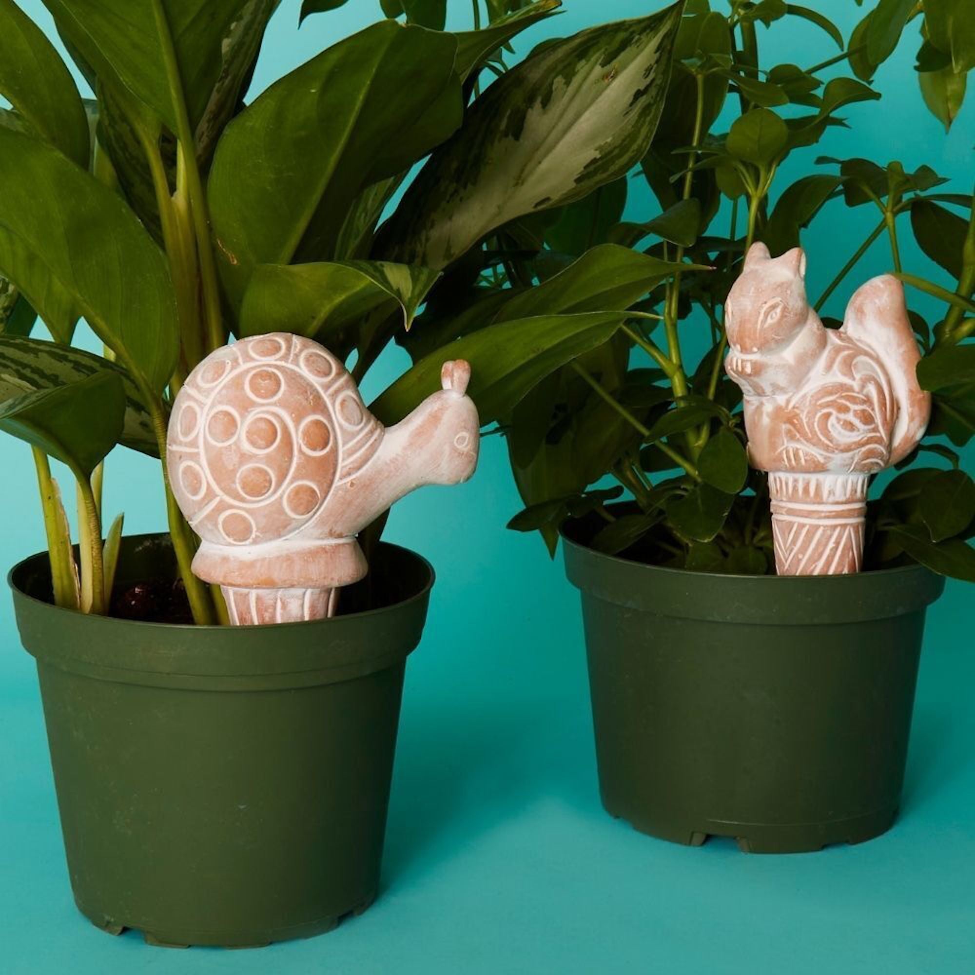 Two terracotta animal watering stakes in a planter with plants
