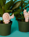 Two terracotta animal watering stakes in a planter with plants