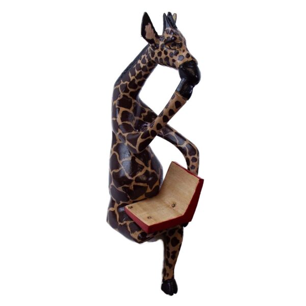 A wooden figurine of a giraffe sitting cross-legged and reading a book