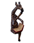 A wooden figurine of a giraffe sitting cross-legged and reading a book