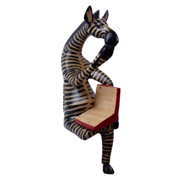 A hand-carved wooden shelf sitter of a zebra sitting cross-legged and reading a book