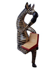 A hand-carved wooden shelf sitter of a zebra sitting cross-legged and reading a book