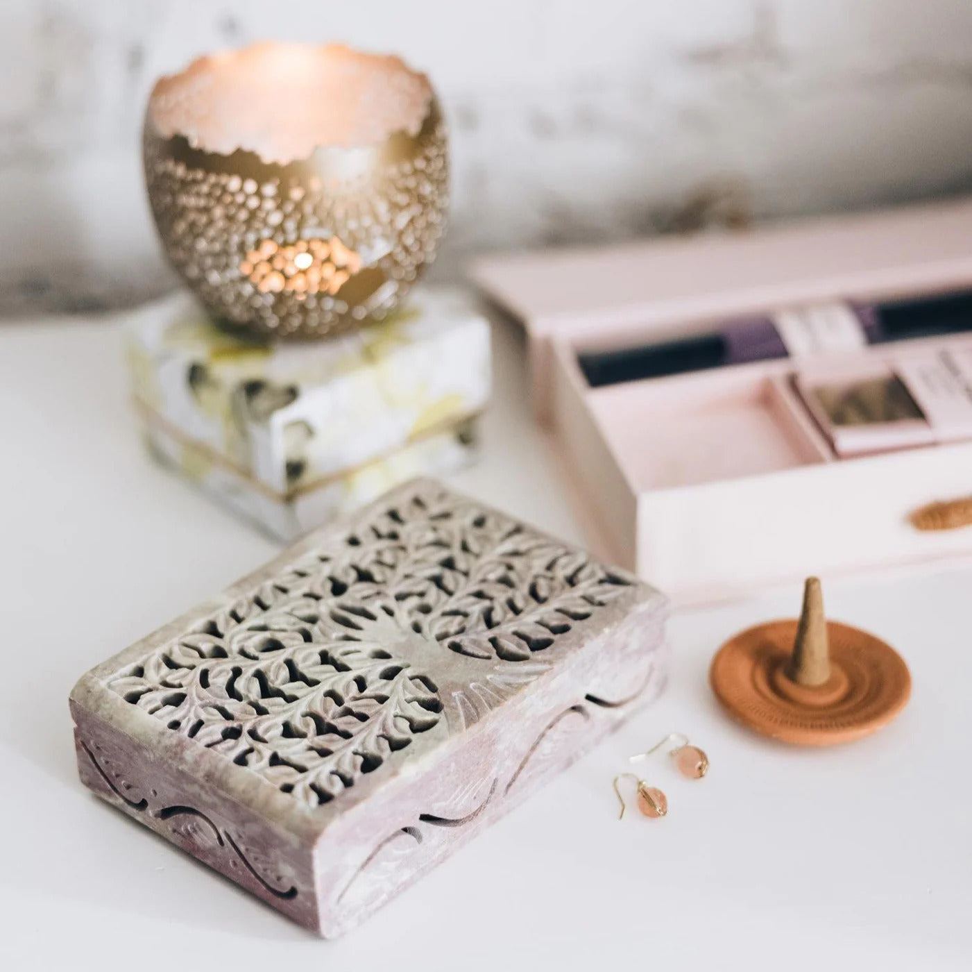 Decorative stone keepsake box with a lit candle and wooden incense holder on a white surface.
