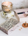 Decorative stone keepsake box with a lit candle and wooden incense holder on a white surface.