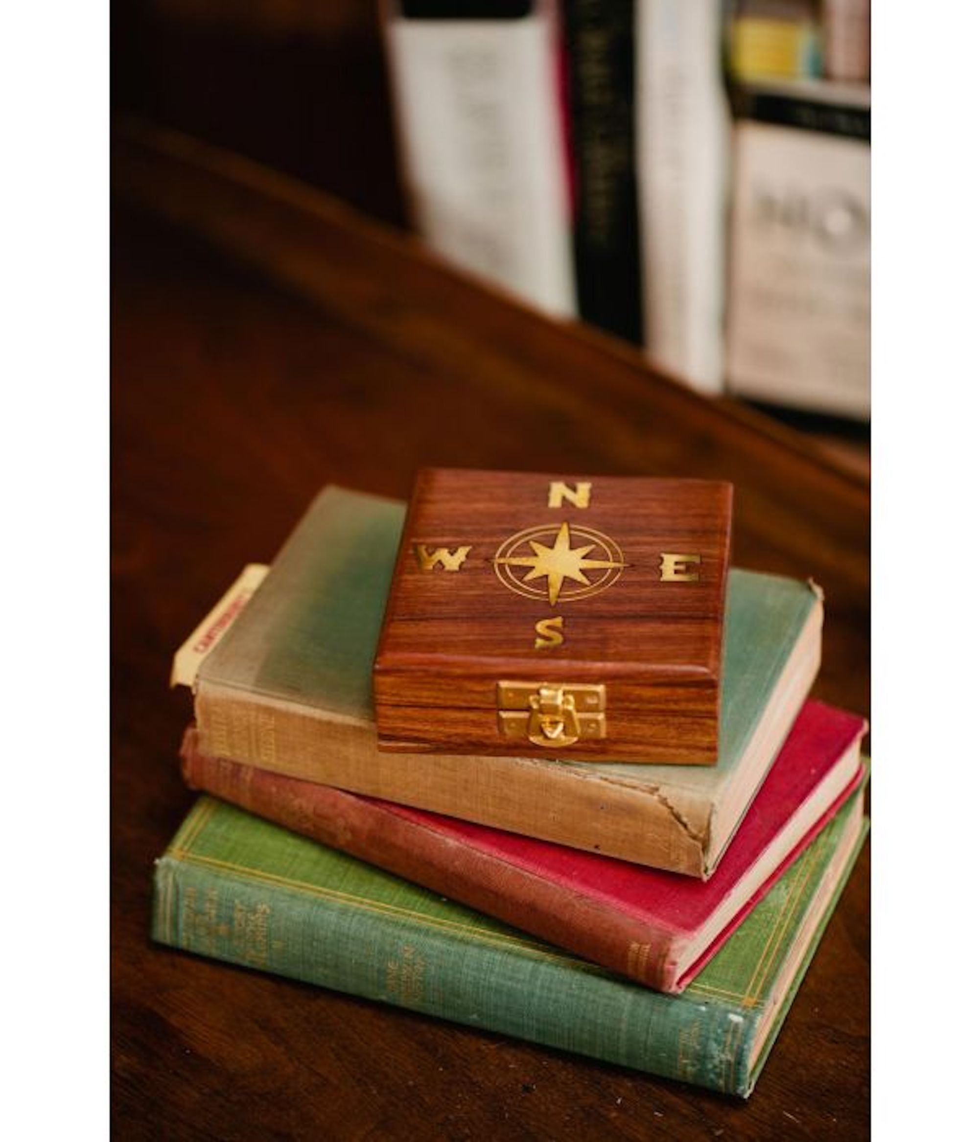 A navigational compass with a sheesham wood box, featuring a metal body and a glass face on top of a stack of books.