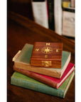 A navigational compass with a sheesham wood box, featuring a metal body and a glass face on top of a stack of books.