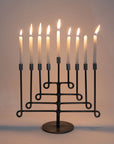 Black metal menorah with lit candles on a plain background